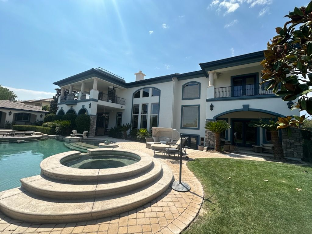 Luxury home with a pool and spa on a sunny day. White exterior, arched windows, and balconies.