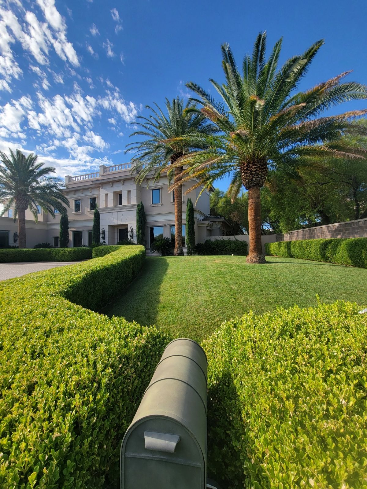 Luxurious home with palm trees, manicured hedges, and blue sky.