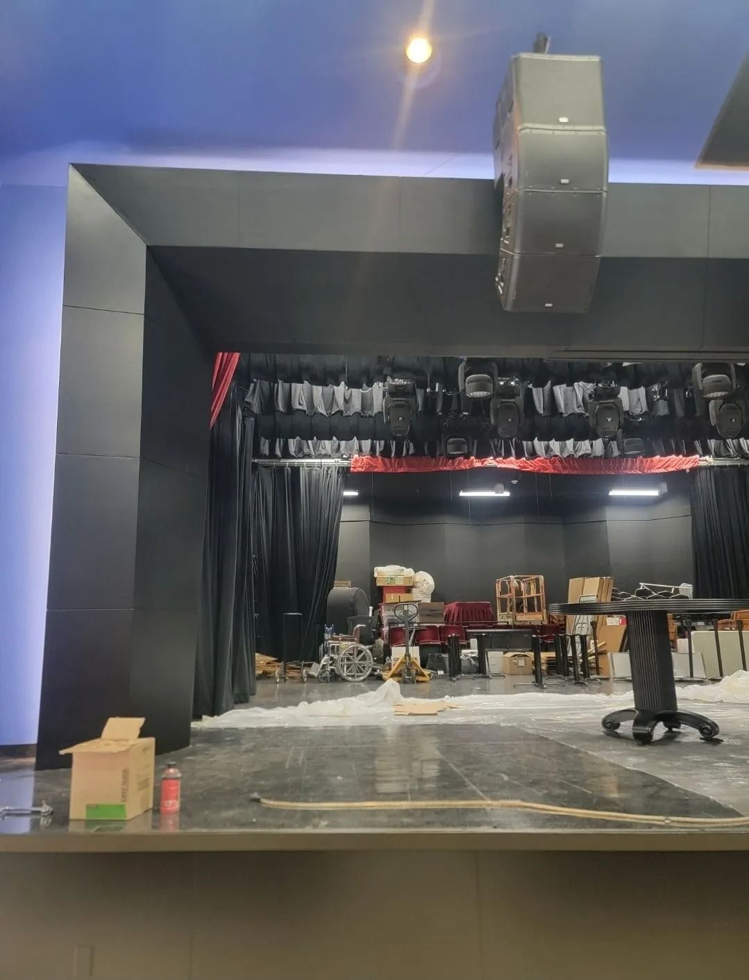 Stage area with black curtains, equipment, and a hanging speaker.