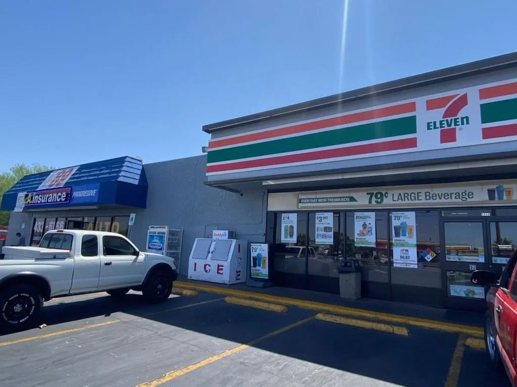 Exterior of a 7-Eleven store and adjacent building. White truck parked in front. Blue sky.