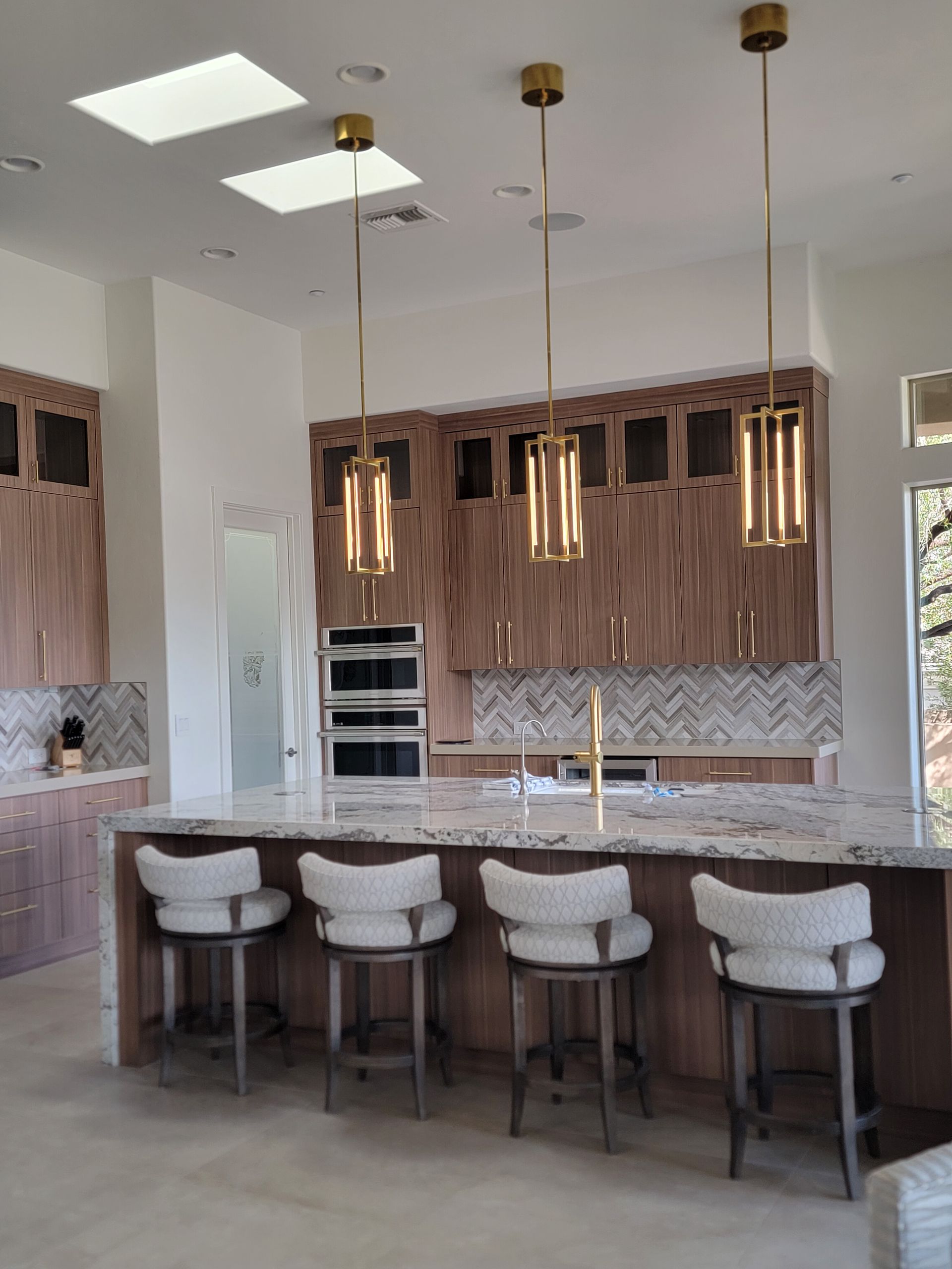 Modern kitchen with island, pendant lights, bar stools, and wooden cabinetry.