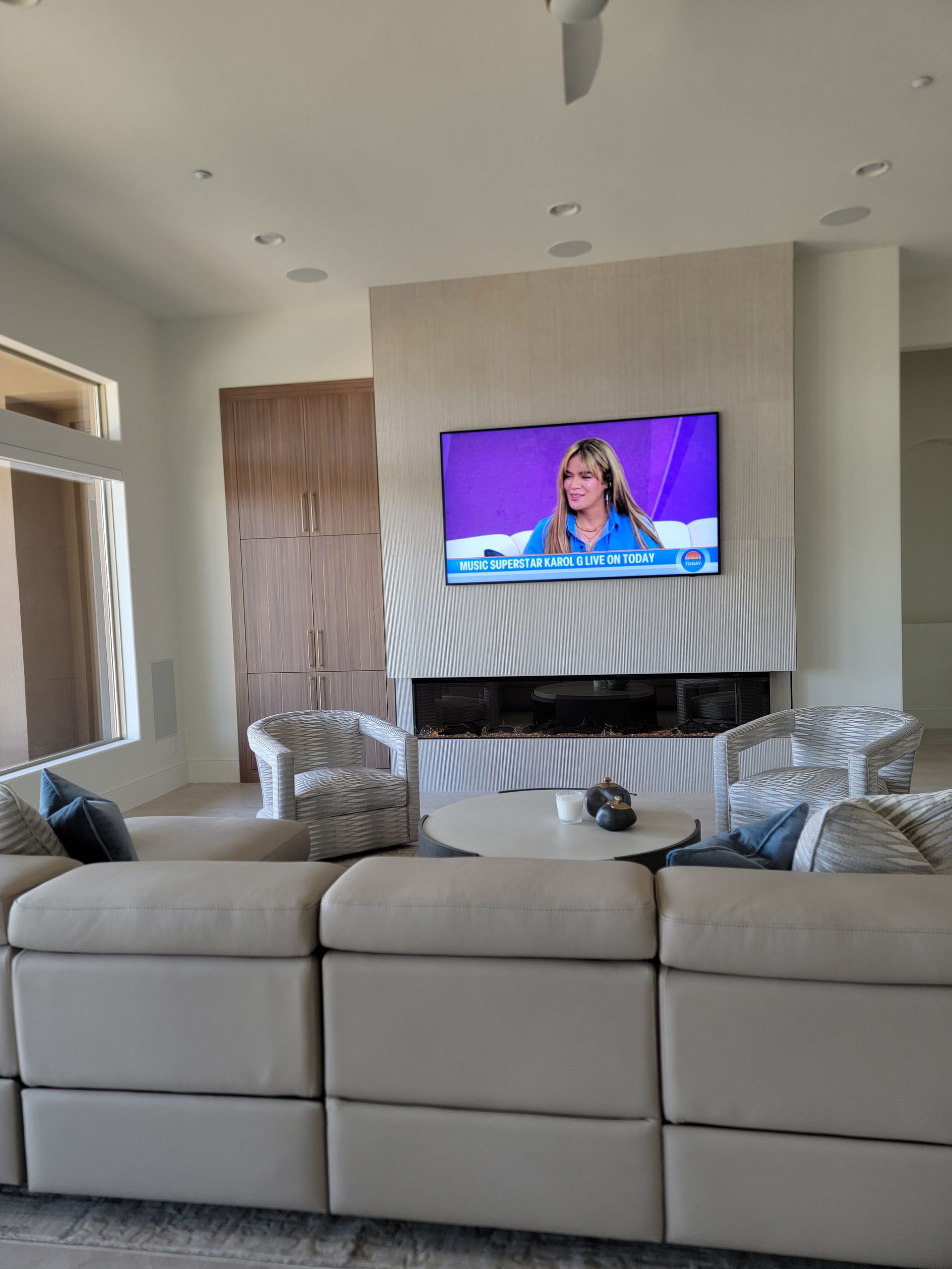 Living room with sectional sofa, fireplace, and TV showing a person on the screen.