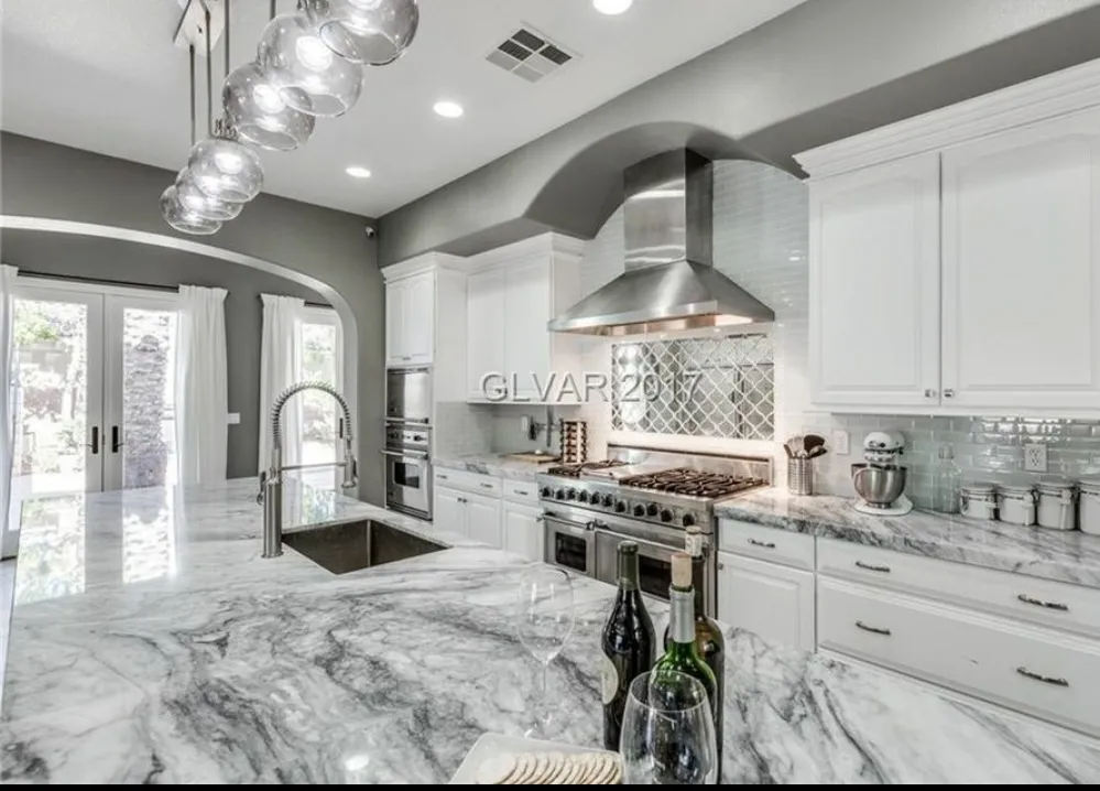 Luxurious white kitchen with marble countertops, stainless steel appliances, and glass pendant lights.