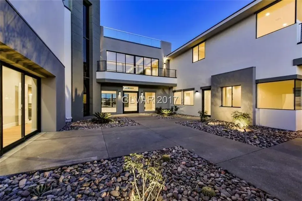 Modern home exterior with gray and white facade, glass doors, and a stone courtyard.