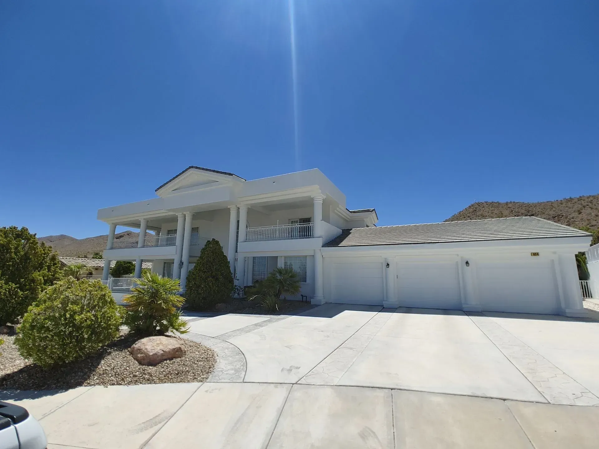 White two-story house with a balcony and a three-car garage on a sunny day.
