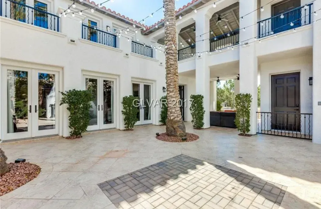 Courtyard of a white stucco mansion with multiple doors and balconies, string lights, and a central palm tree.