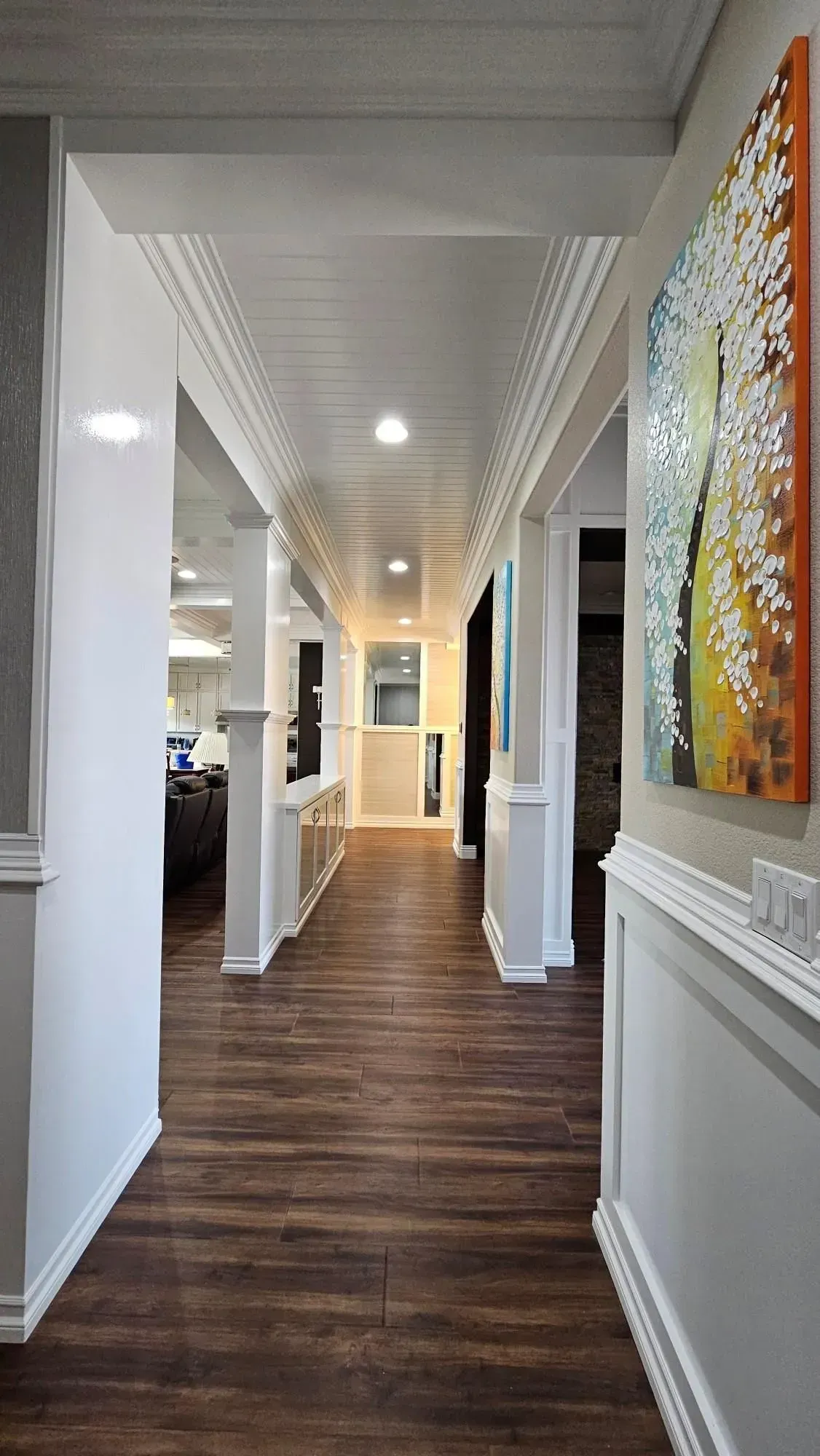 Hallway with dark wood floor, white columns, and art on the wall.