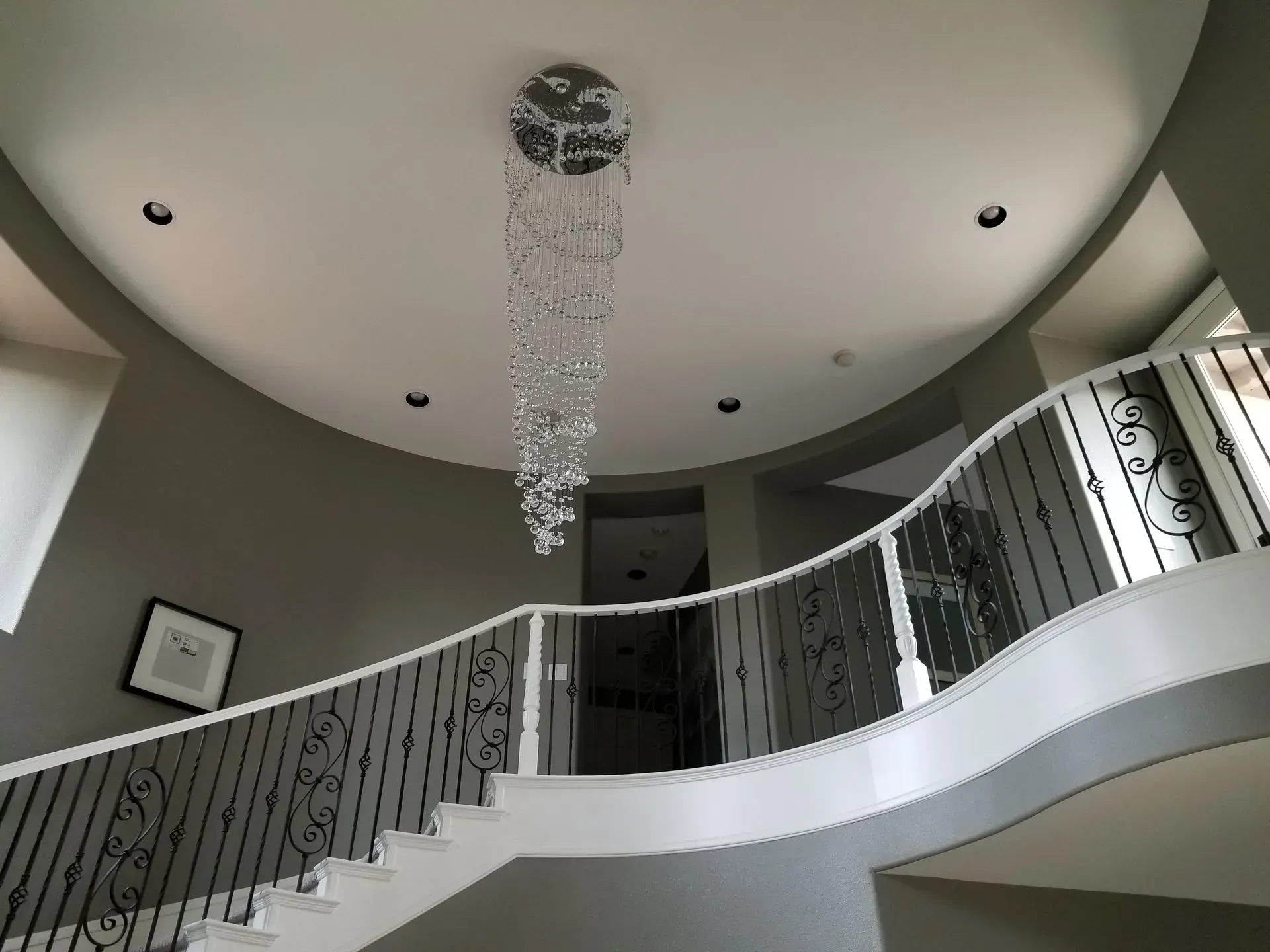 Grand foyer with a spiral staircase, chandelier, and gray walls.