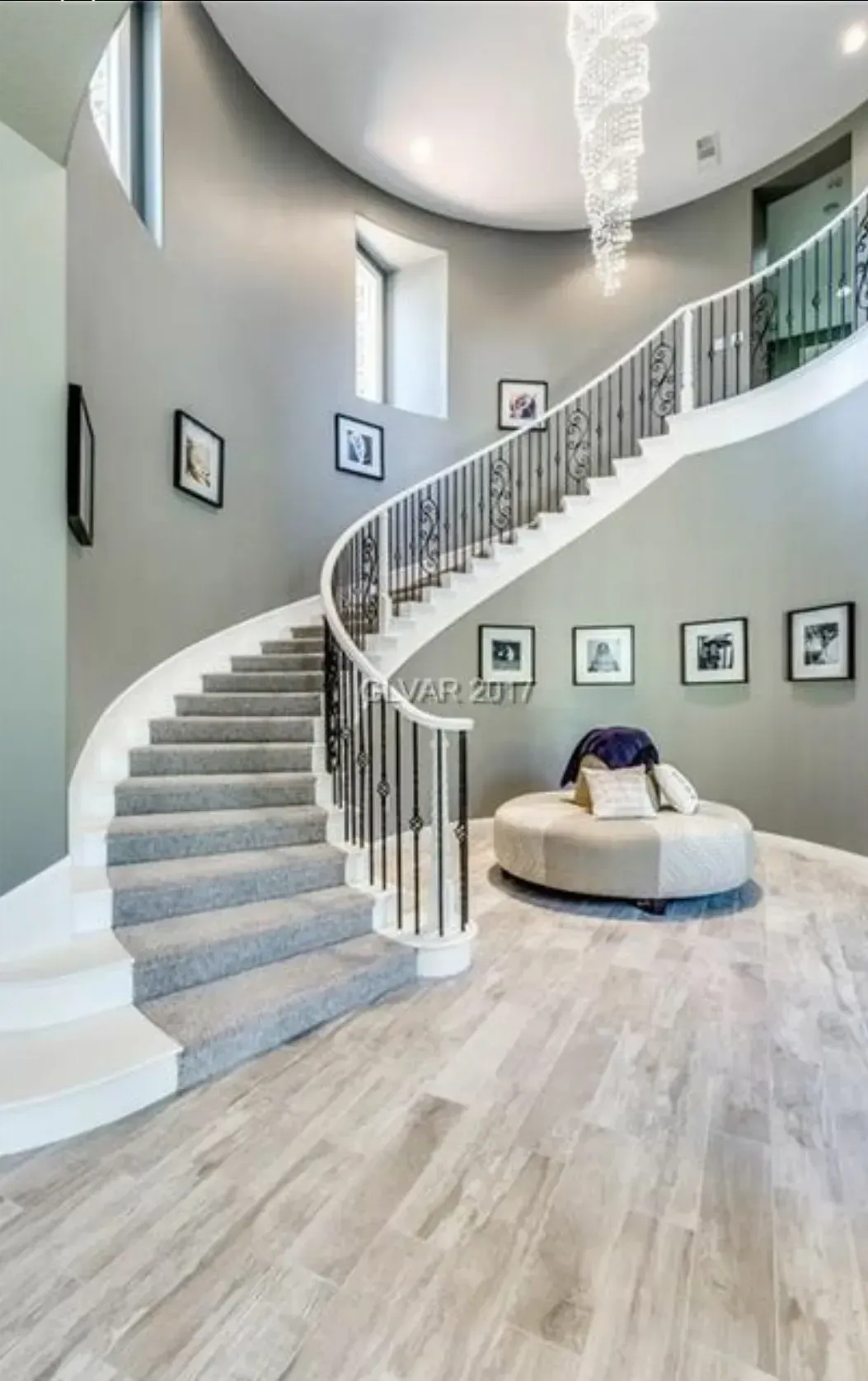 Curving staircase with gray carpet and white trim. Wooden flooring, gray walls, and a round seating area.