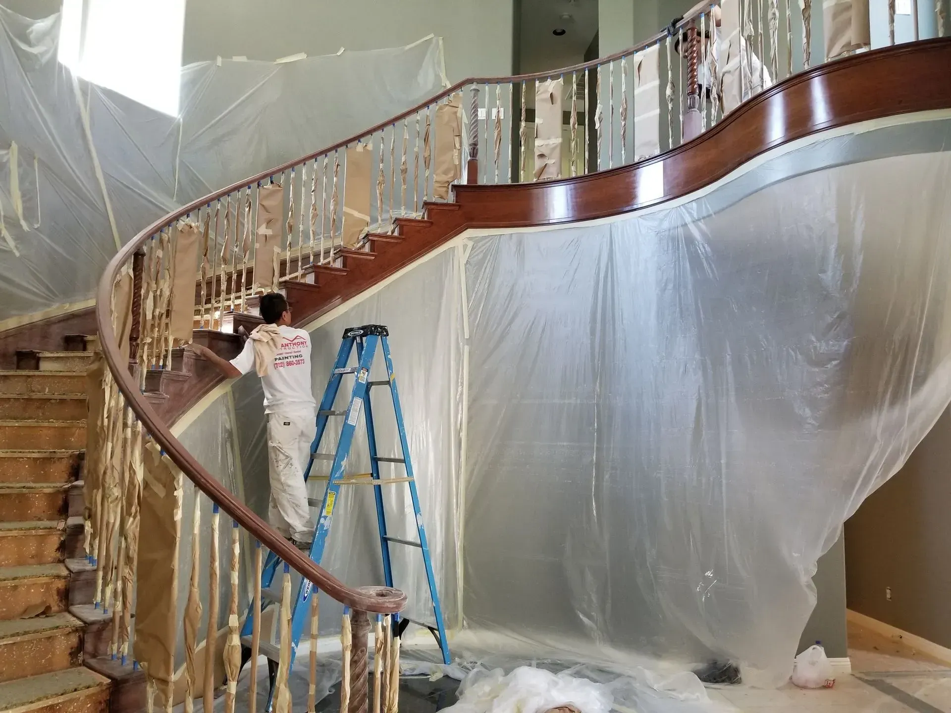 Person painting a curved staircase, covered in plastic sheeting.