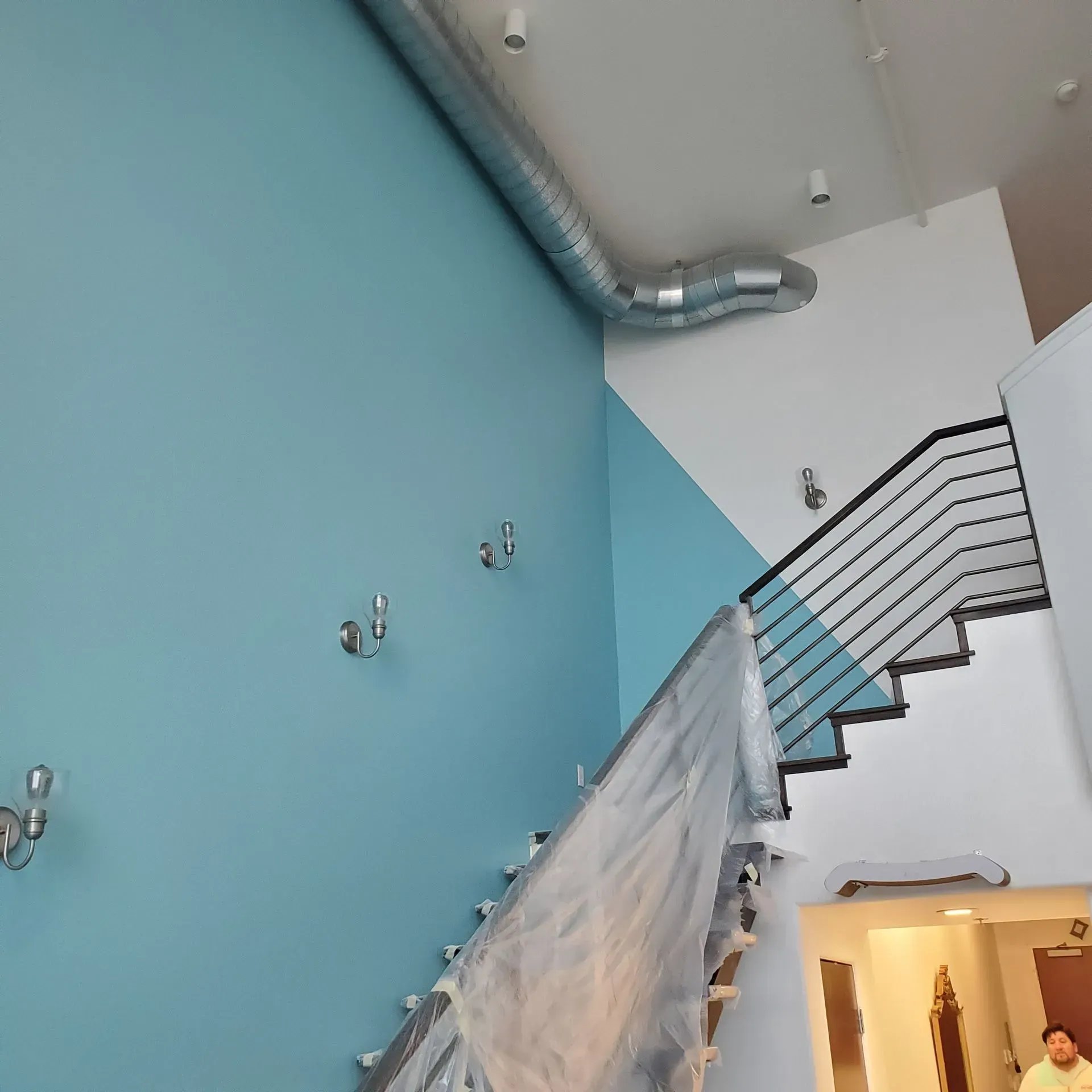 Blue and white painted stairwell with metal railing, ductwork, and sconces.
