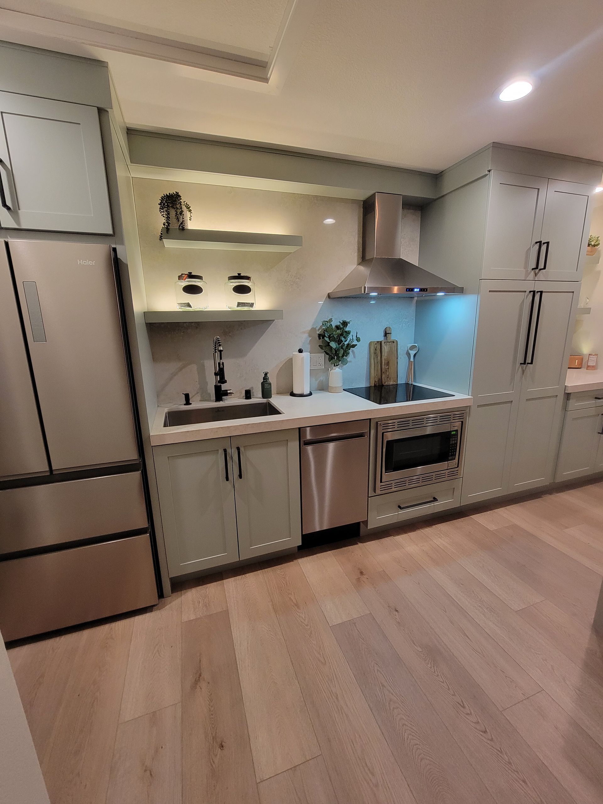 Modern kitchen with light green cabinets, stainless steel appliances, and wood flooring.