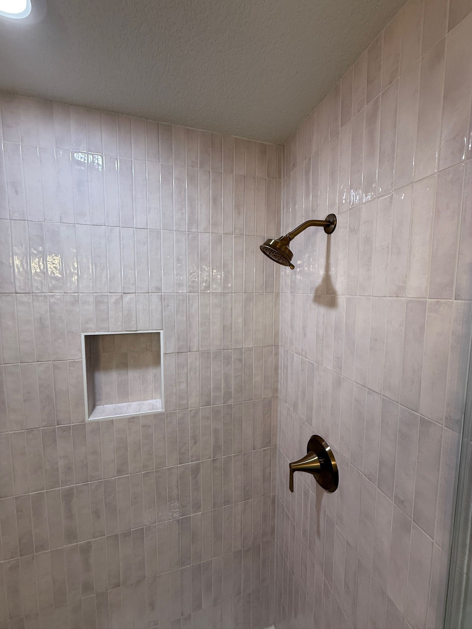 Shower stall with beige tile walls, two bronze shower heads, and a recessed soap niche.