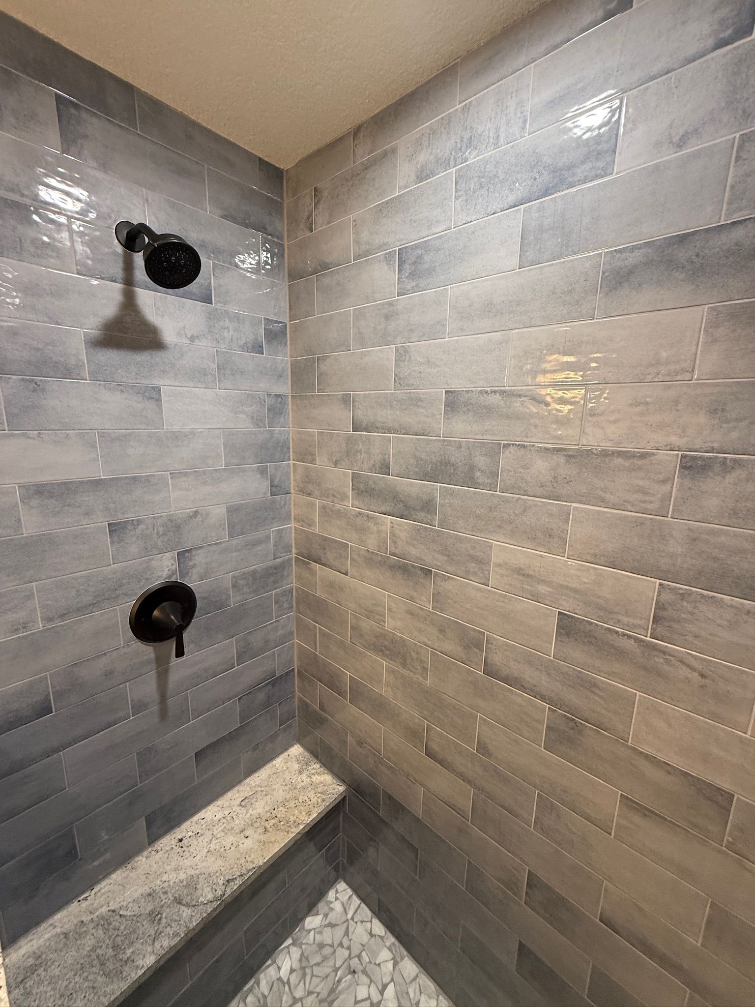 Tiled shower corner with two black wall fixtures and a built-in corner shelf.