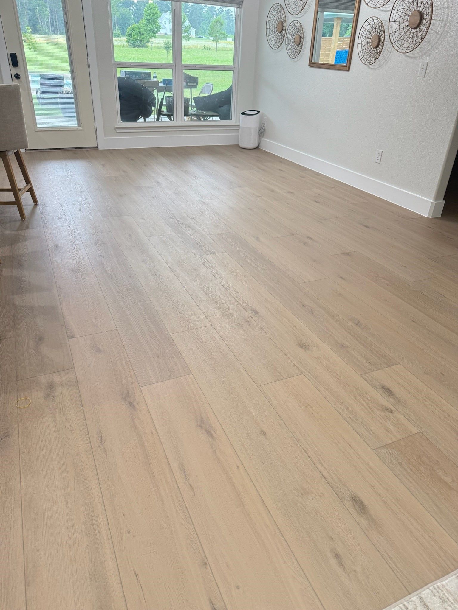 Empty living room with light wood flooring, gray walls, and sliding glass doors opening to a patio.