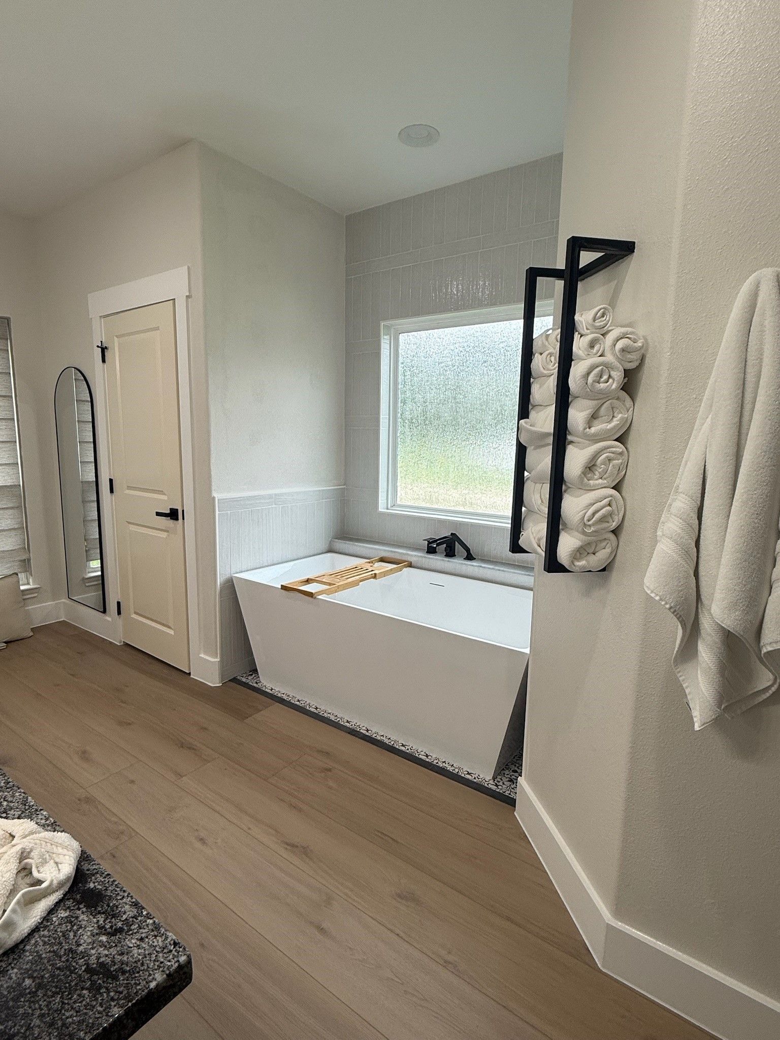 Small bright bedroom with a bed by the window, wall hooks, and wood floors