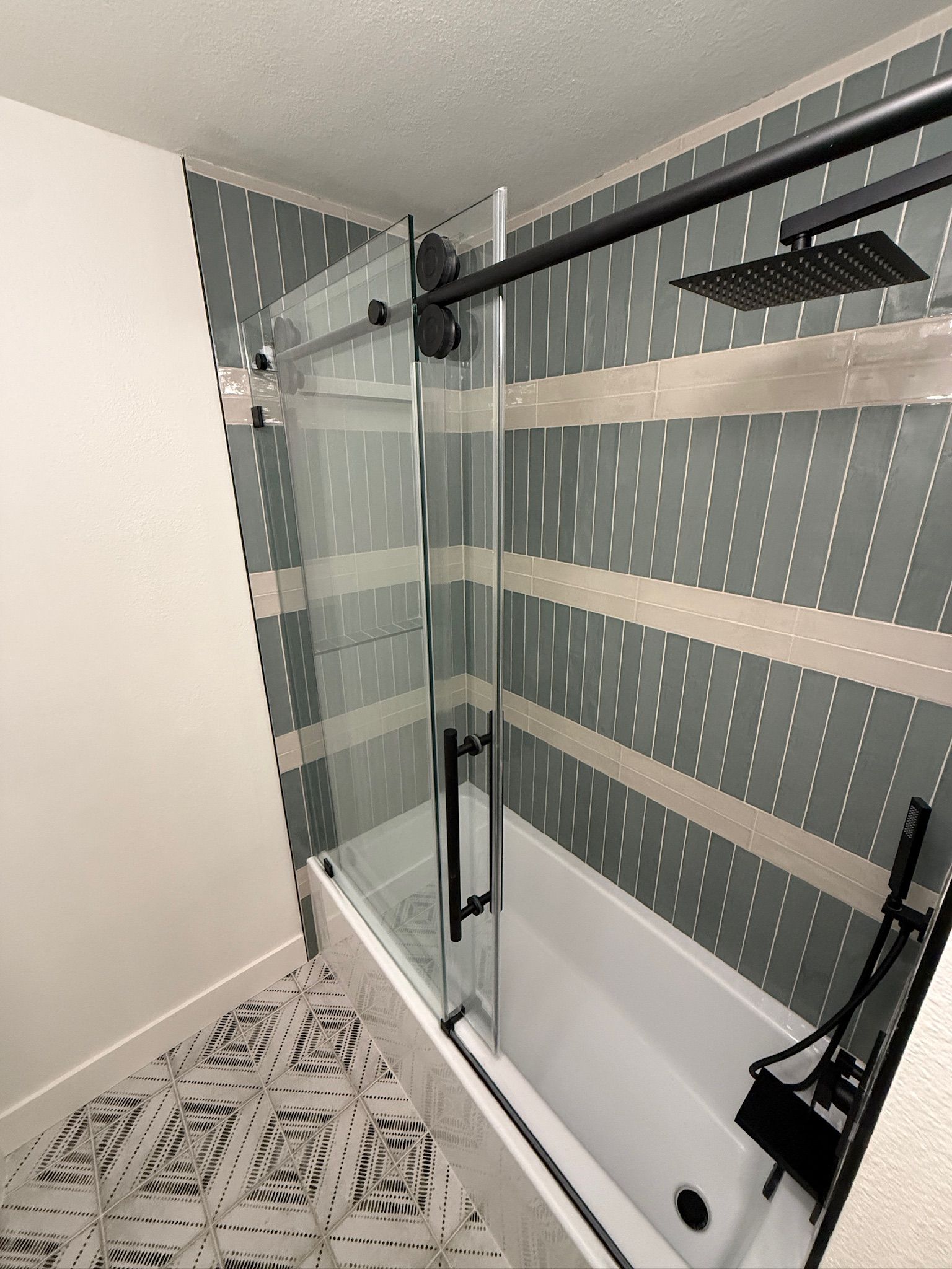 Modern shower stall with glass doors, black fixtures, striped gray wall panels, and patterned floor tiles