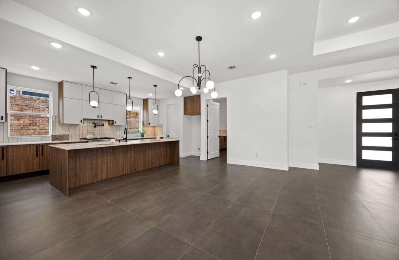 Open-concept modern kitchen and living area with wood cabinets, dark tile floor, and white walls