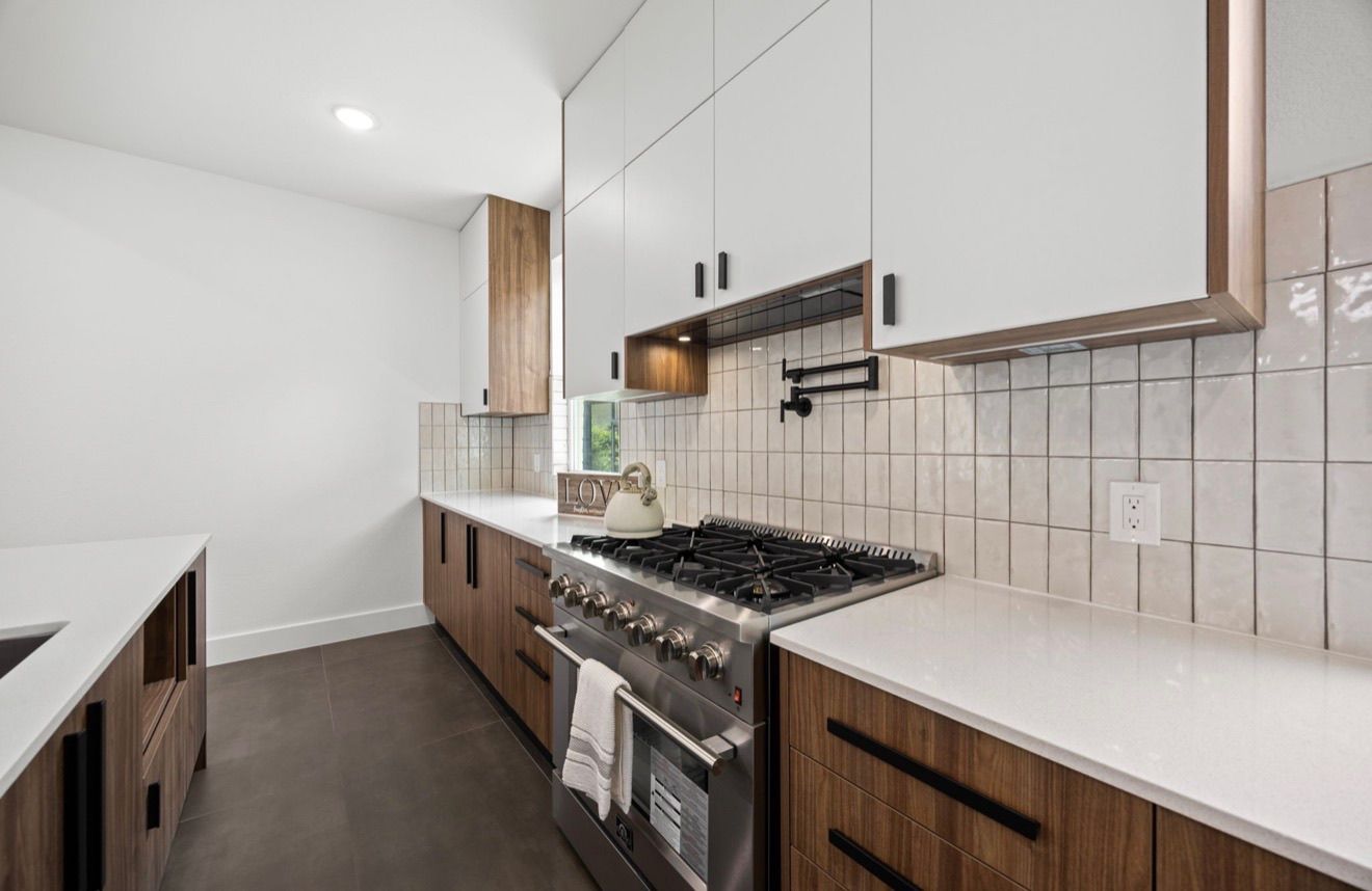 Modern galley kitchen with white cabinets, wood accents, gas range, and subway tile backsplash