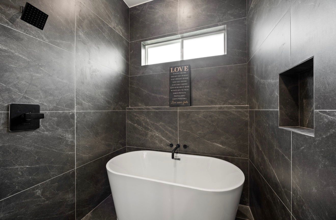 Modern shower with dark gray tiled walls and a white freestanding tub beneath a window
