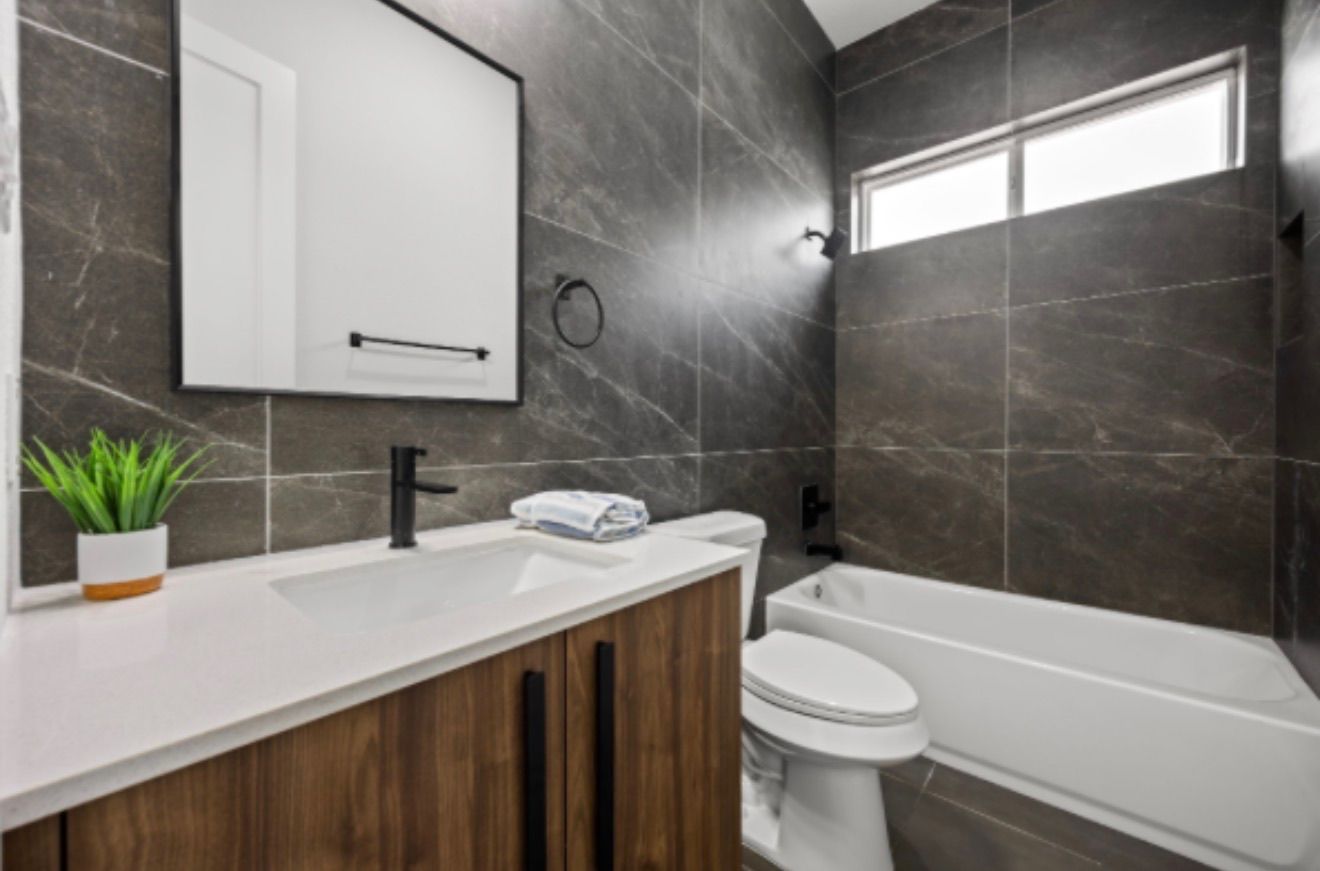 Modern bathroom with dark tile, wood vanity, white sink, toilet, and bathtub