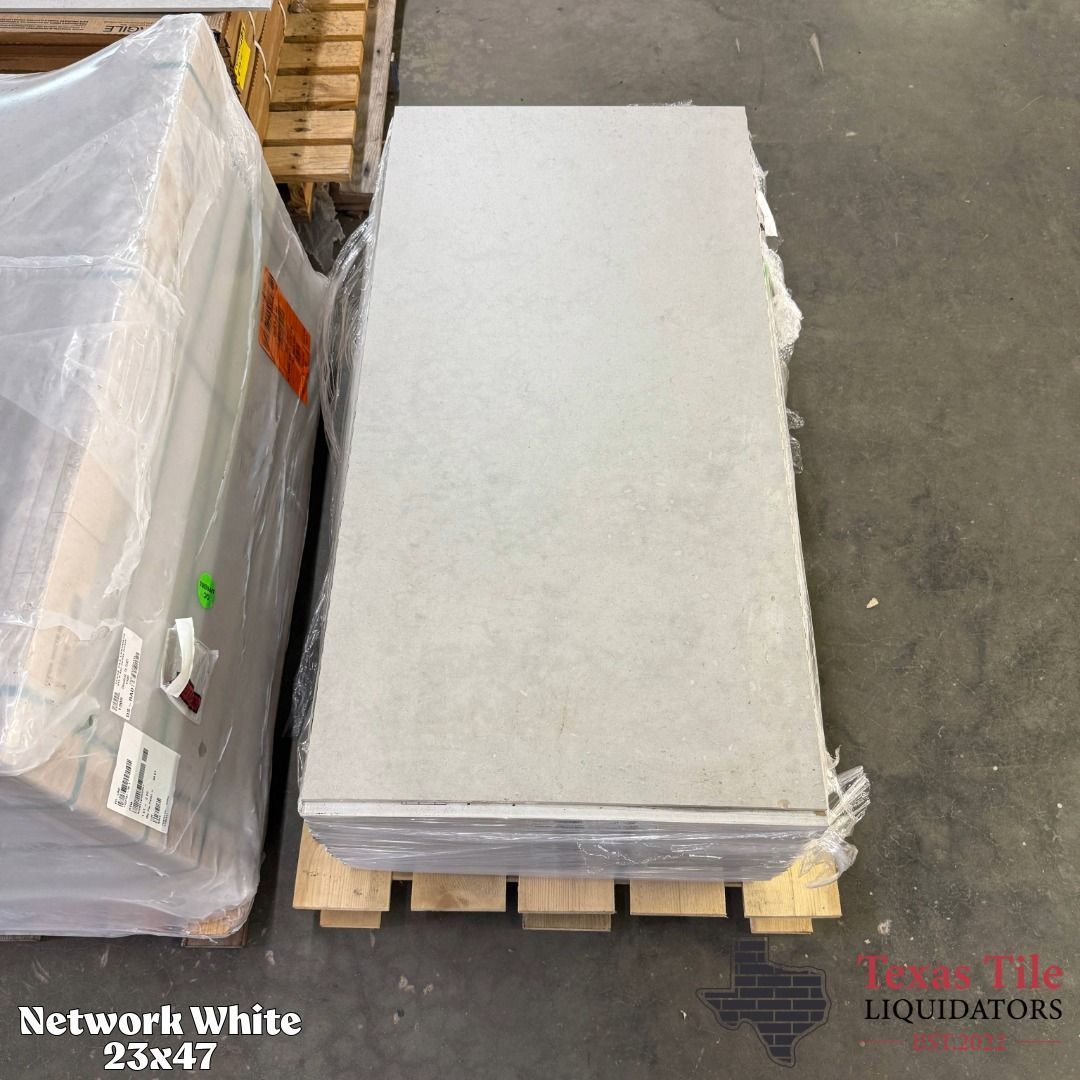 Stacked white tile slabs on a wooden pallet in a warehouse aisle