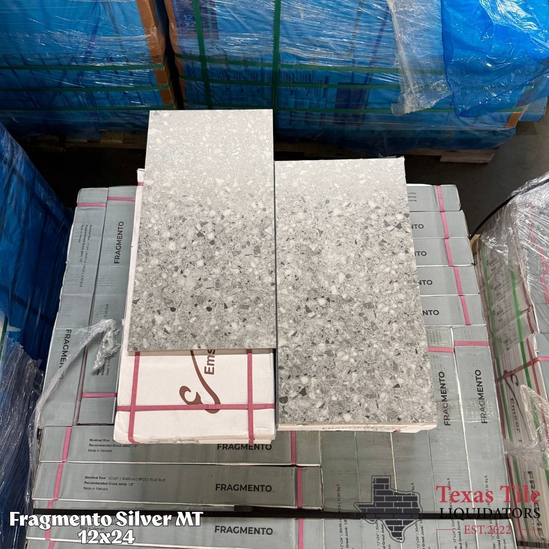 Two speckled gray tile samples resting on stacked boxes in a warehouse setting