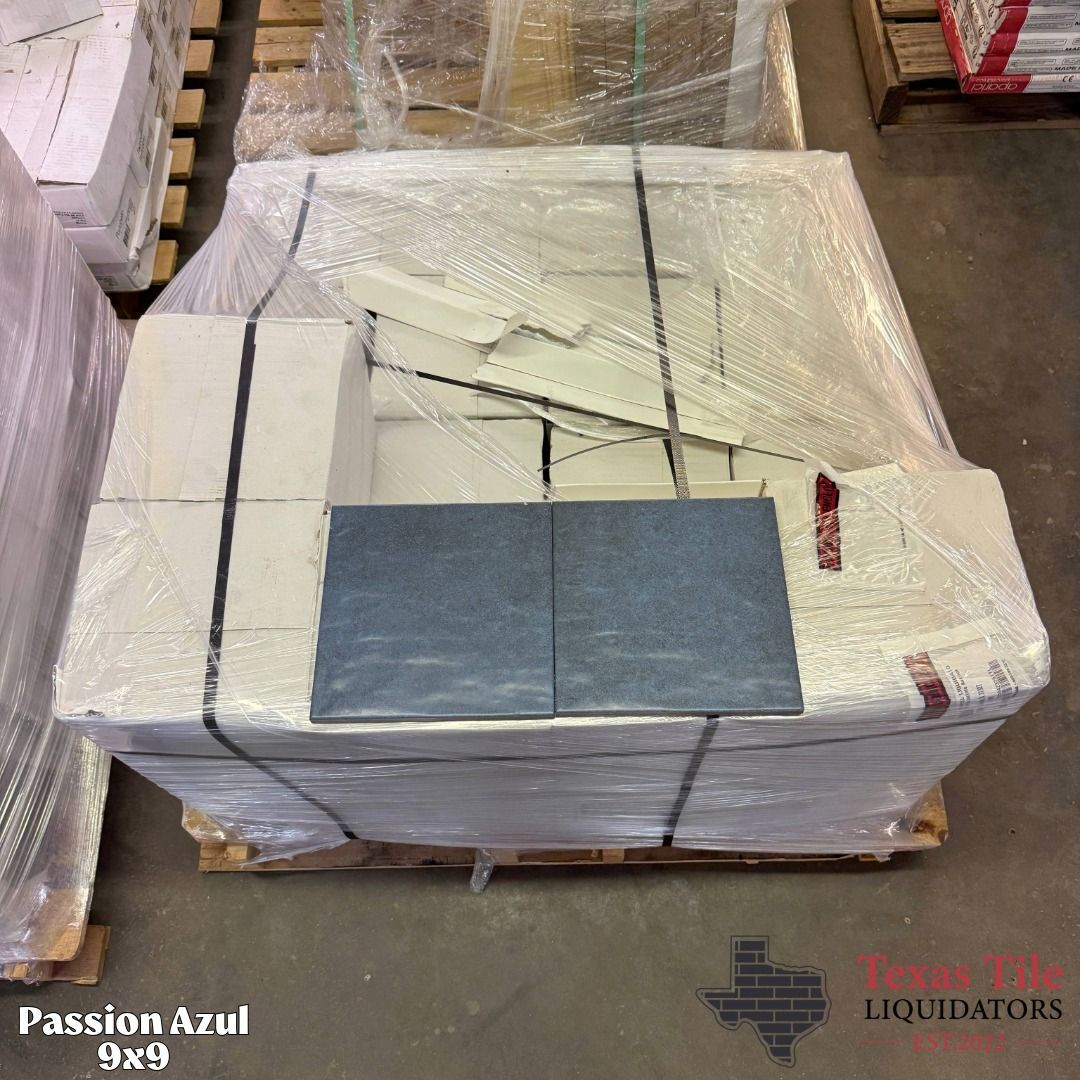 Wrapped pallet of white panels with two blue-gray tiles on top in a warehouse setting