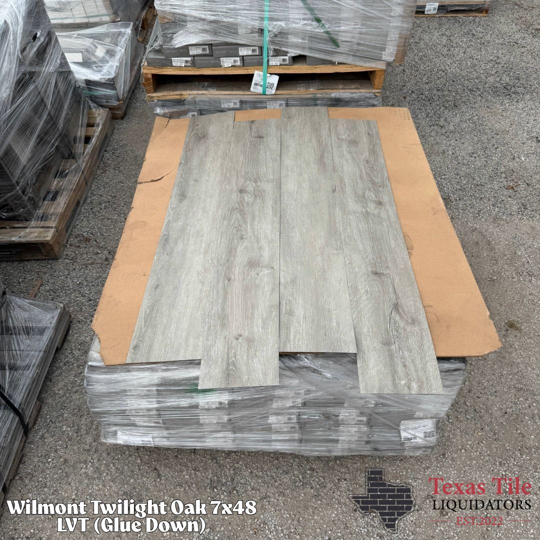 Stacked oak-look flooring planks on a pallet in a warehouse, with packaging labeled Wilmont Twilight Oak 7x48.