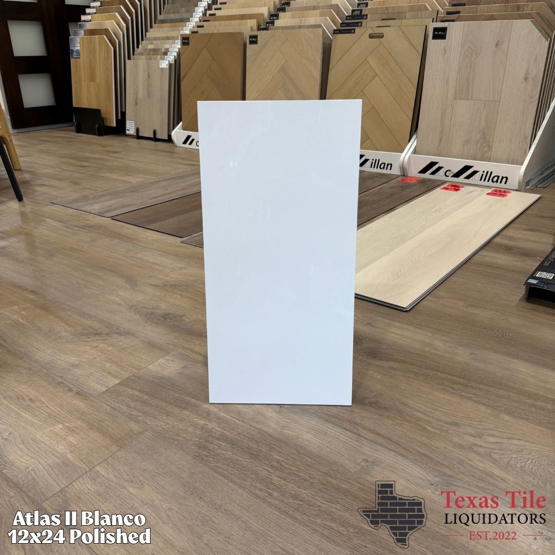 White rectangular tile standing upright on a wood floor in a tile showroom, with sample tiles displayed behind it.