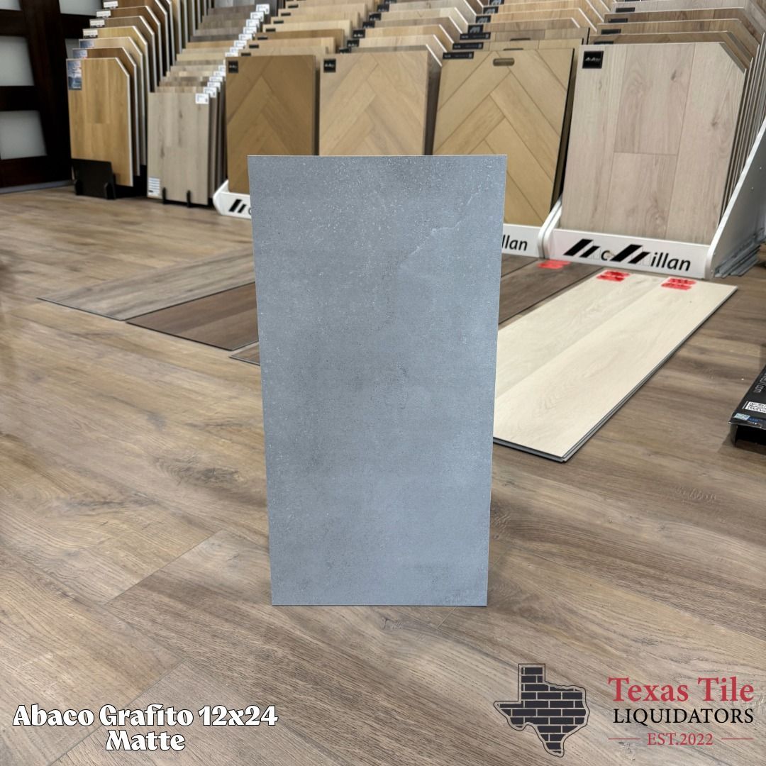 Gray rectangular tile display in a tile showroom, with wood-look samples in the background