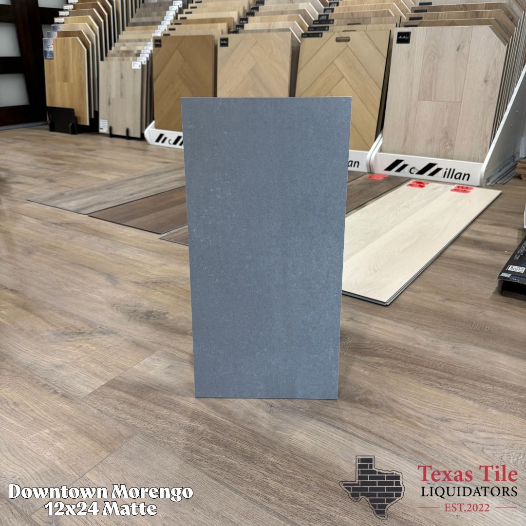 Gray rectangular tile standing upright in a tile showroom, with flooring samples displayed behind it