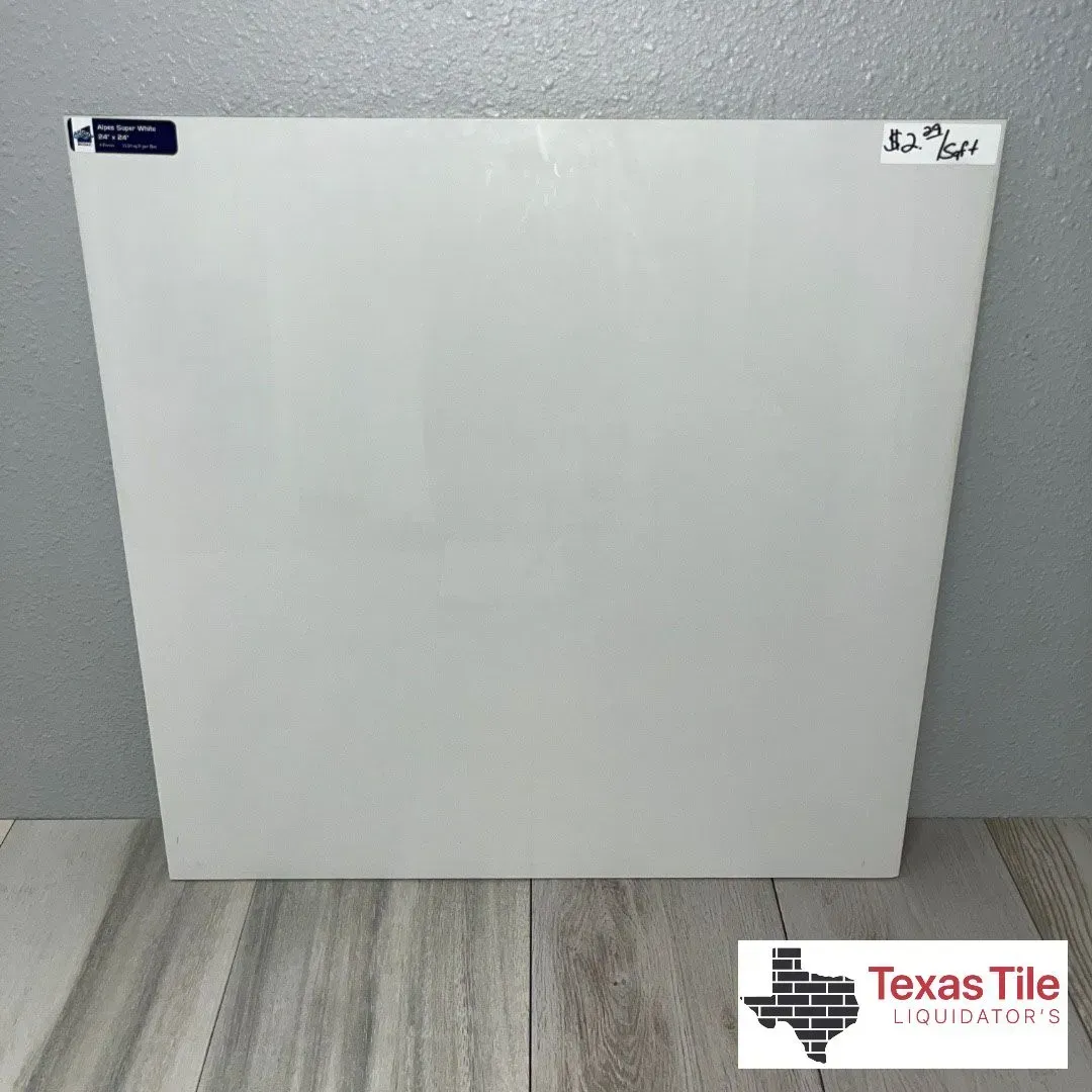 A square, plain white glossy tile sample positioned against a gray wall, featuring a Texas Tile Liquidators logo.