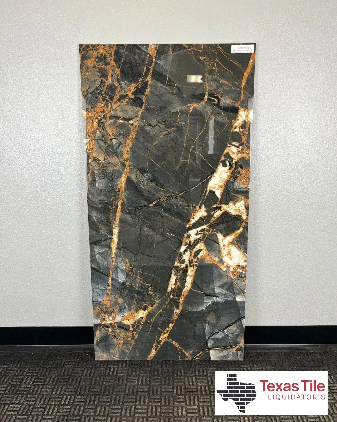 A vertical rectangular slab of dark gray marble tile with prominent gold and white veining, displayed on a floor stand.