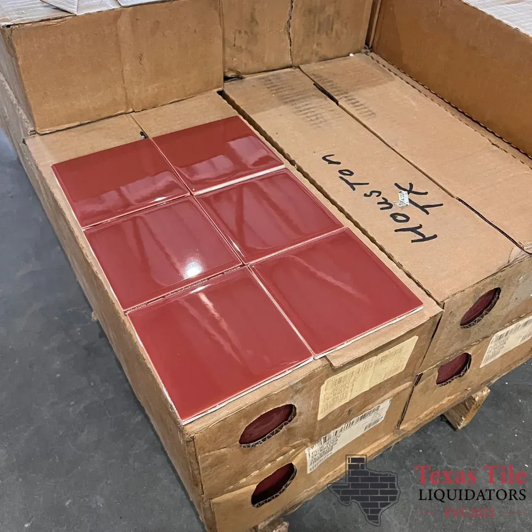 A shipping pallet holds several cardboard boxes of glossy, red square tiles, with one box open revealing its contents.