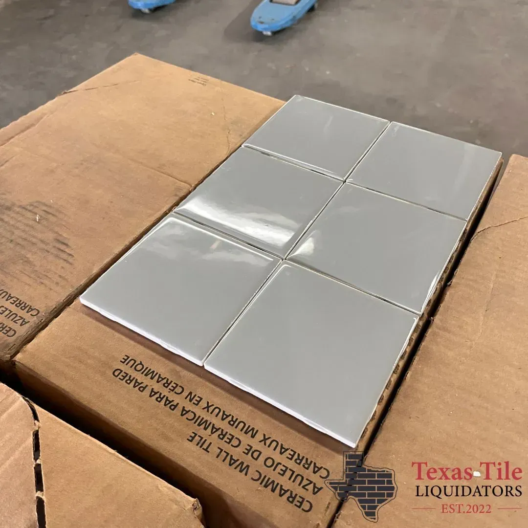 A grid of six glossy light gray square ceramic wall tiles sitting on top of their cardboard packaging box.