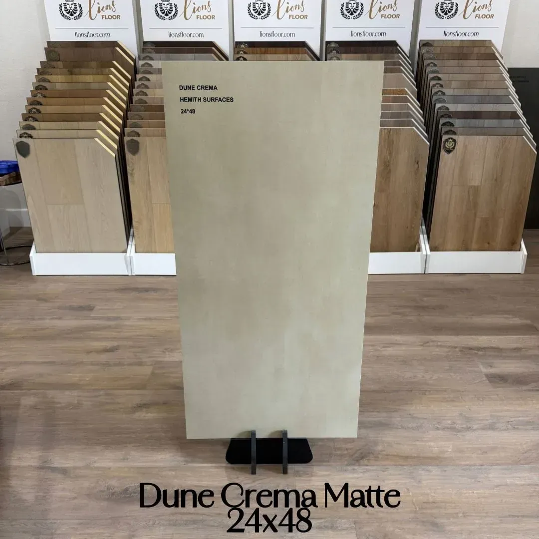 A tile sample titled Dune Crema Matte 24x48 stands on a display rack in a flooring showroom.