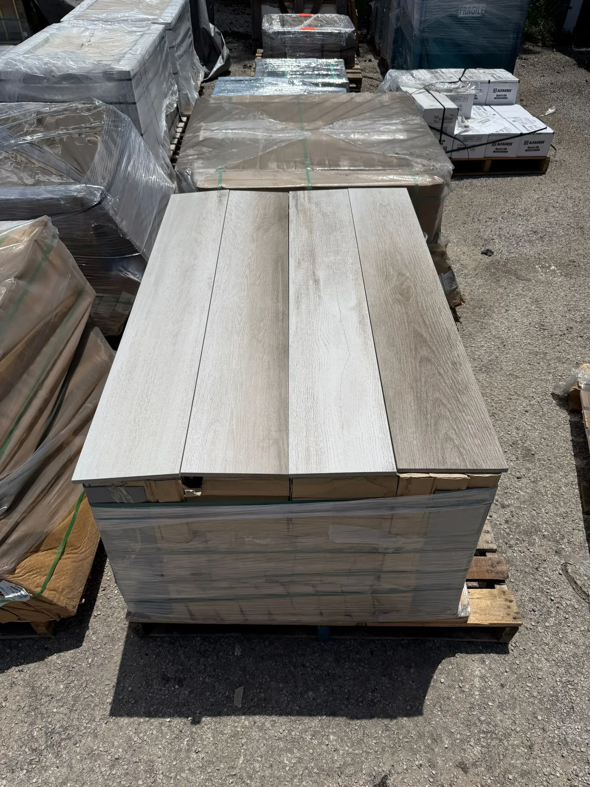 A stack of light brown, wood-look rectangular tiles sitting on a wooden pallet in an outdoor storage yard.