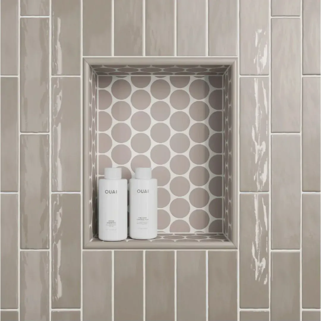 A shower niche with taupe circular tiles and two white shampoo bottles, set against a background of vertical taupe tiles.