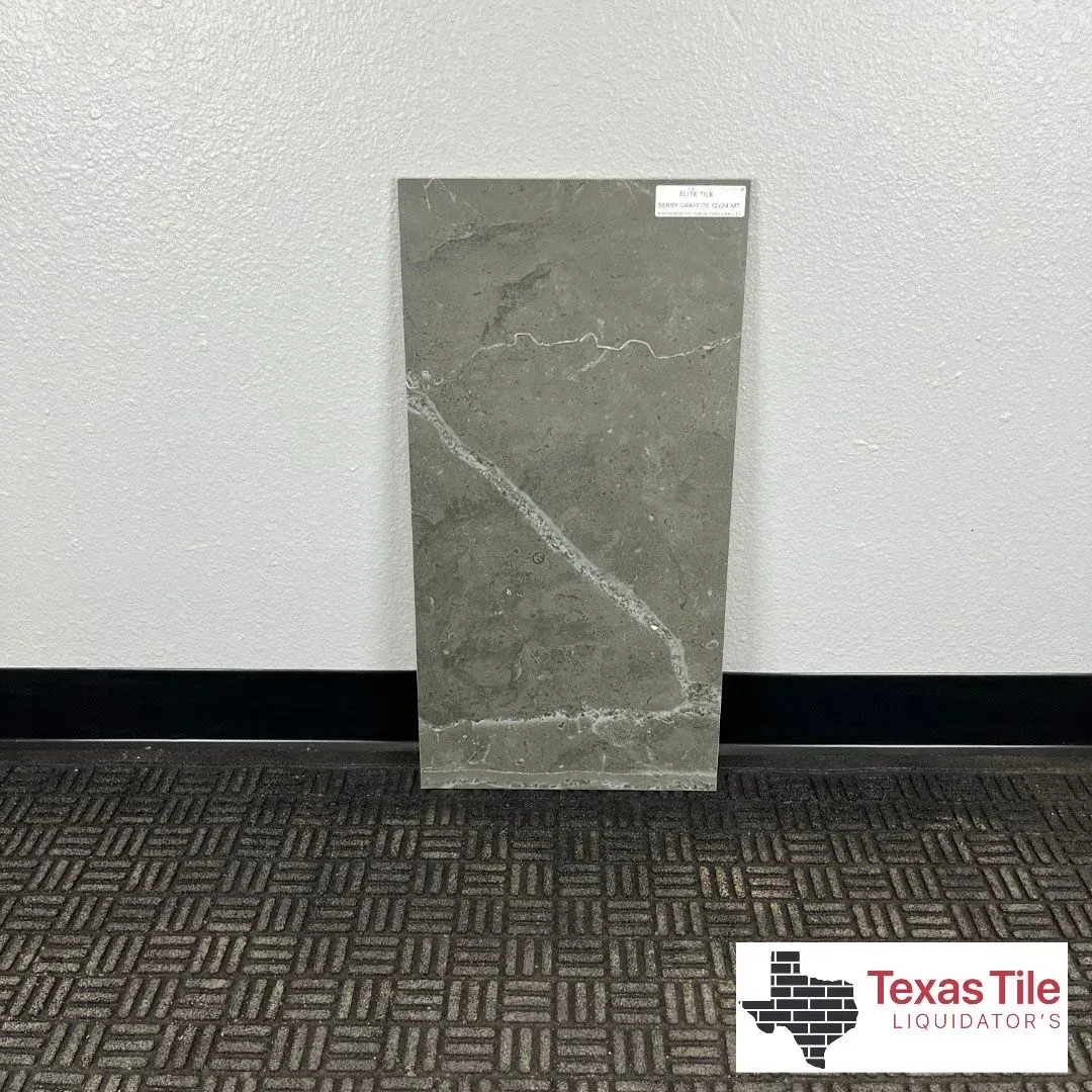 A rectangular, slate-gray floor tile with a prominent white veining pattern, displayed against a wall on a carpeted floor.
