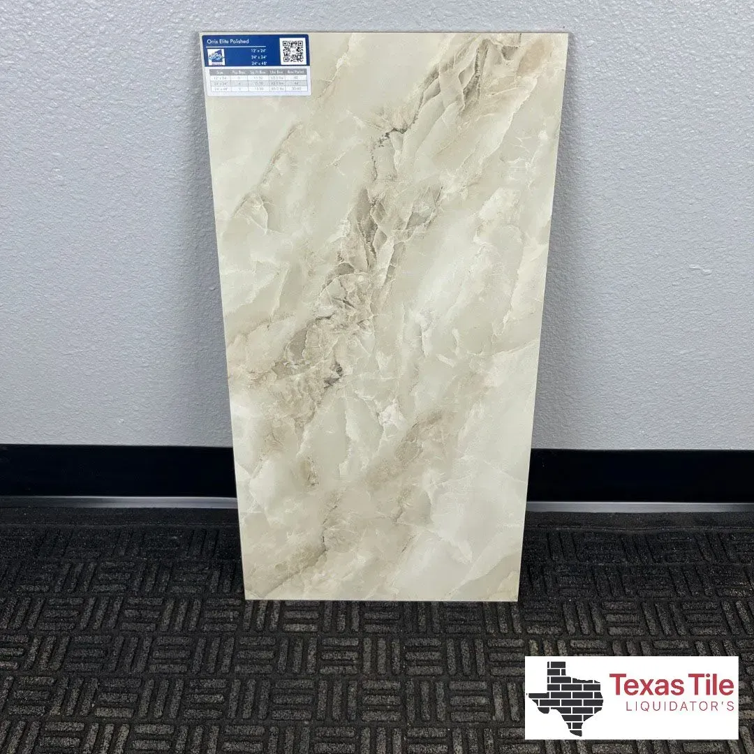 A light beige, marble-look ceramic tile standing upright against a grey wall with a small logo in the bottom corner.