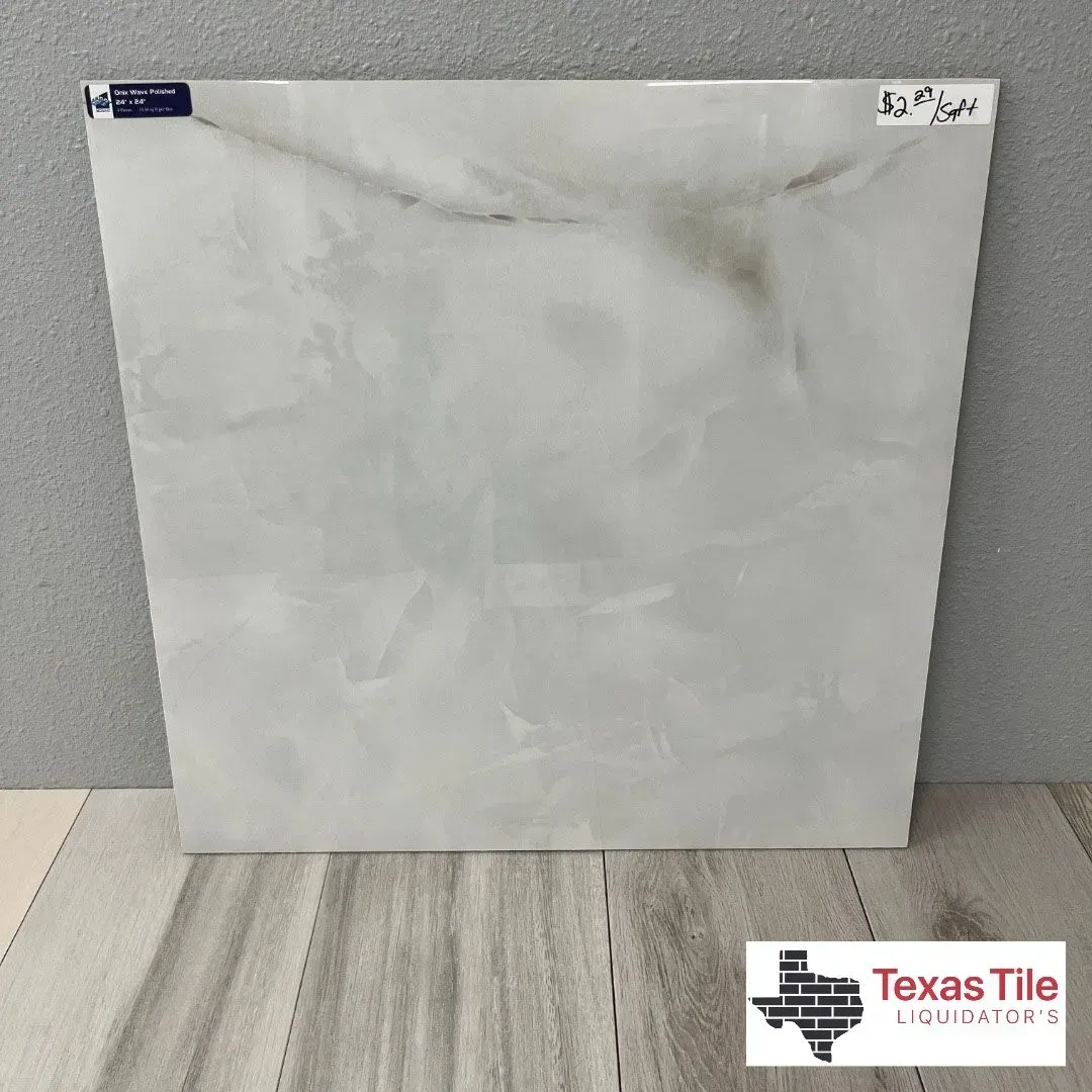 A square, off-white marble-look floor tile displayed against a gray wall, featuring a Texas Tile logo in the corner.