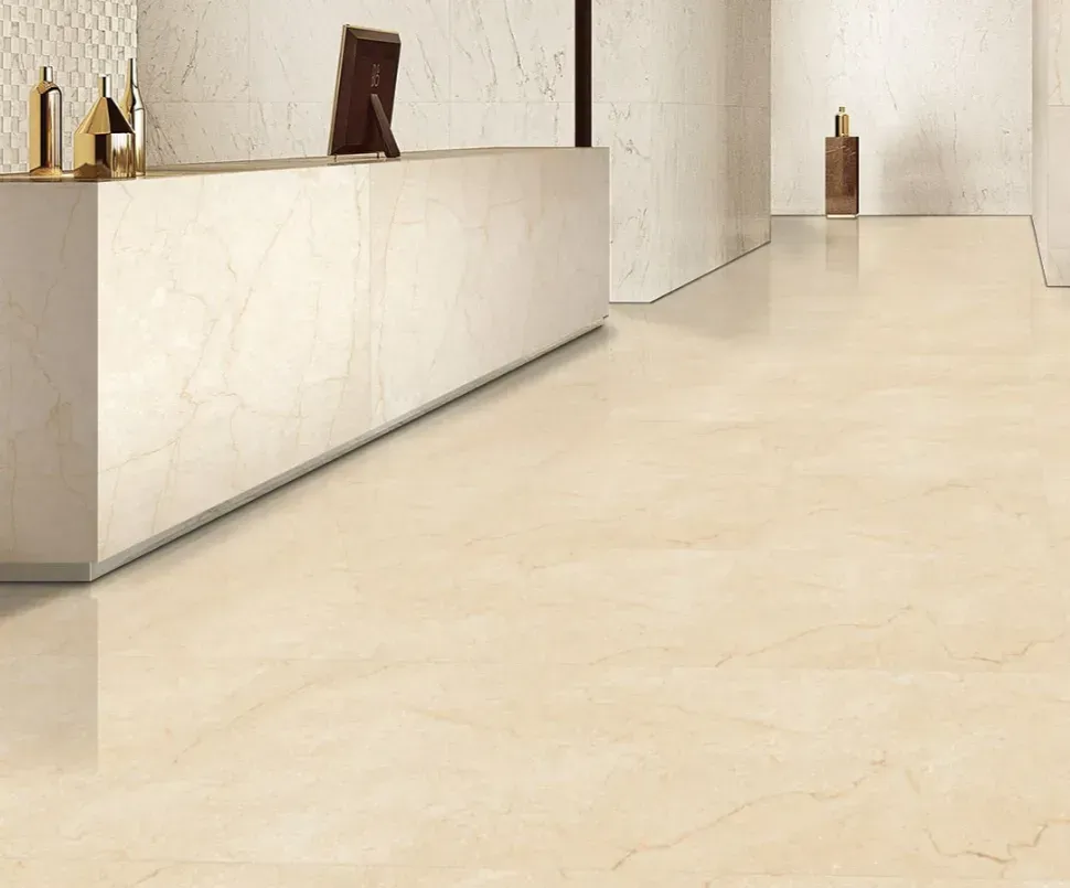 A bright, modern lobby with a long, cream-colored marble reception desk and matching tile flooring.