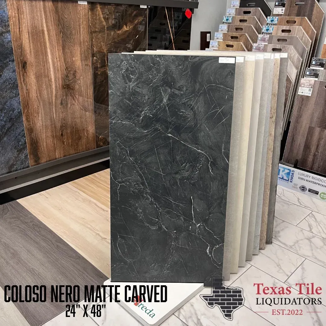 Dark matte carved stone-look tile display in a showroom, with sample boards behind it.