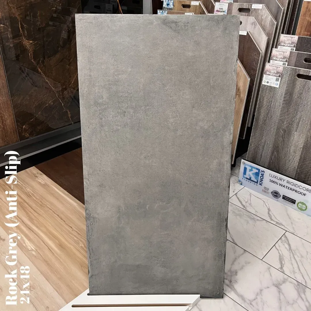 A grey, textured, anti-slip tile sample displayed upright in a showroom.