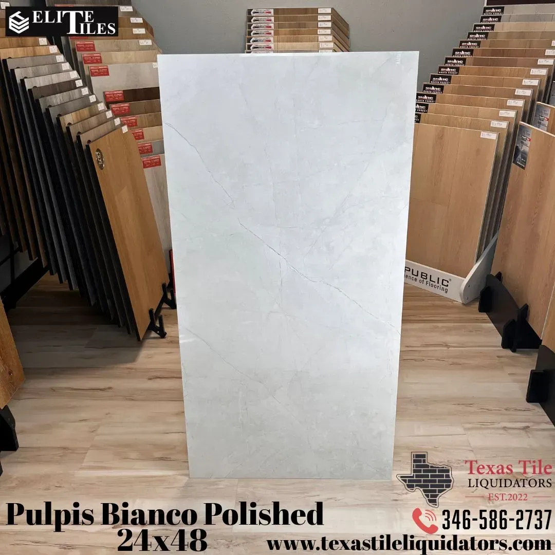 A large, rectangular, white-veined marble-look tile sample stands in a tile showroom, labeled Pulpis Bianco Polished 24x48.