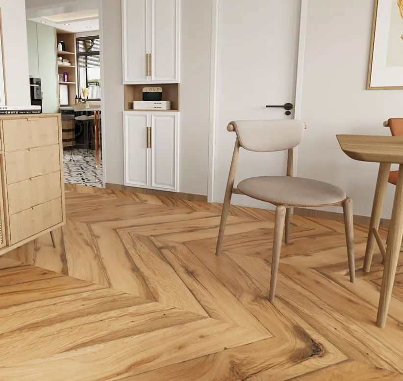 A dining area featuring a light wood table and chair on a chevron-patterned wooden floor, with white cabinetry nearby.
