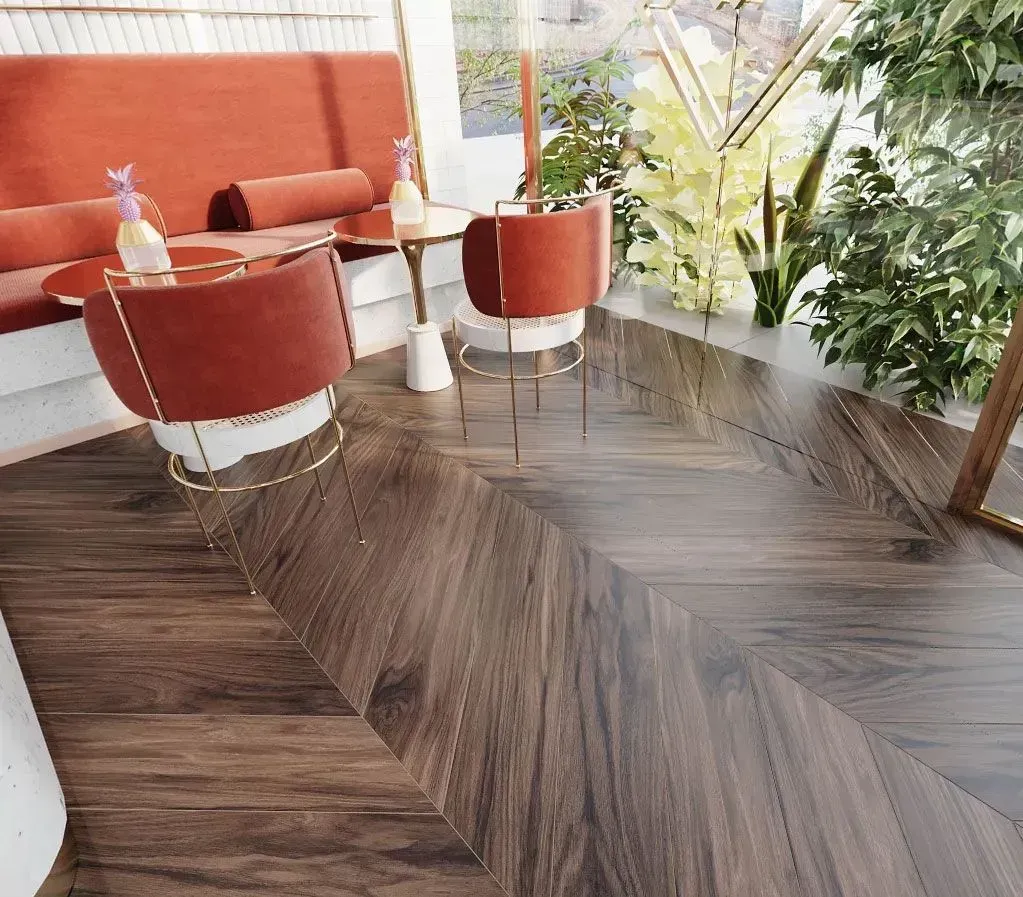 A modern café corner with burnt-orange velvet chairs, small tables, and a dark wood floor laid in a chevron pattern.