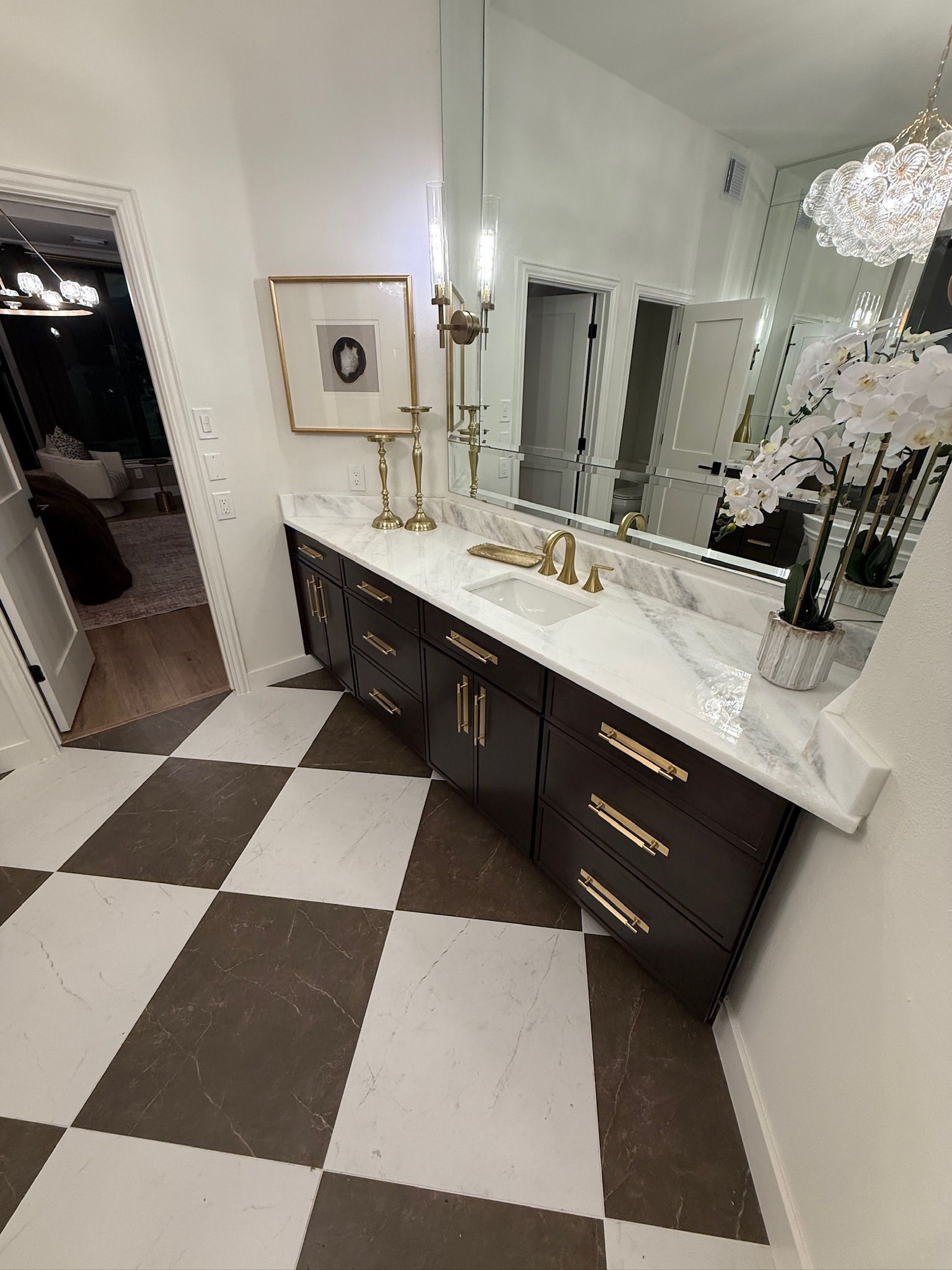 A modern bathroom vanity with dark cabinetry, white marble countertops, gold hardware, and a checkered tile floor.