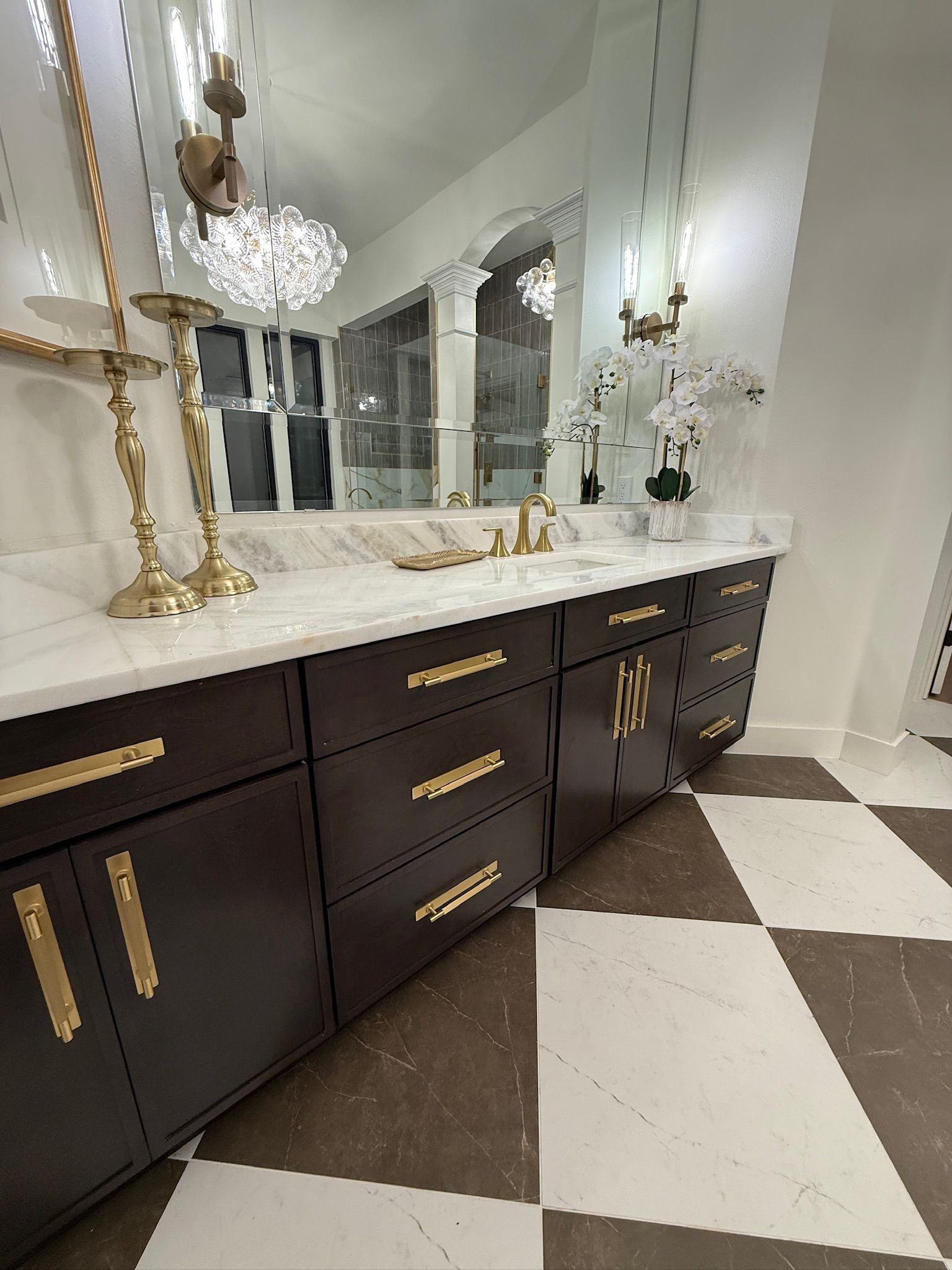 A modern bathroom vanity with dark wood cabinets, gold hardware, and a white marble countertop, set against checker floors.